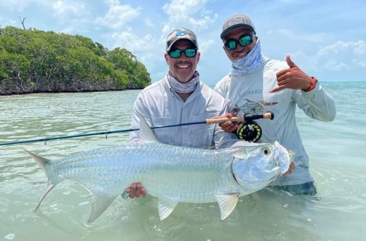 Two anglers standing in caribbean waters holding up a large tarpon fish.