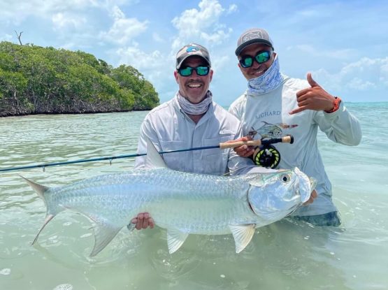 Two anglers standing in caribbean waters holding up a large tarpon fish.