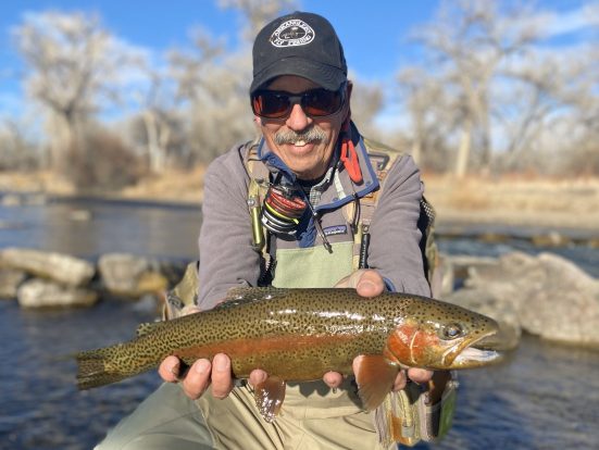 A guest holds a large rainbow trout while on his knee in the river.